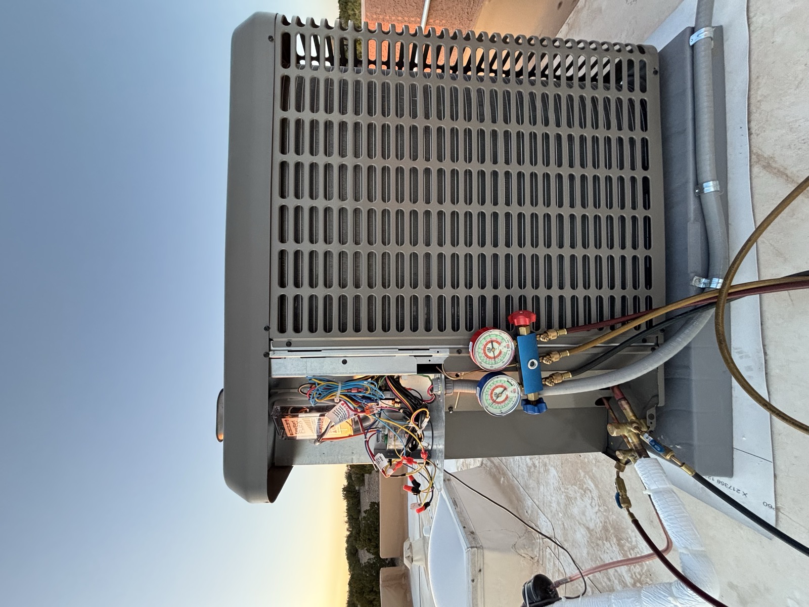 A&J HVAC technician's gauges on a rooftop condenser unit at sunset